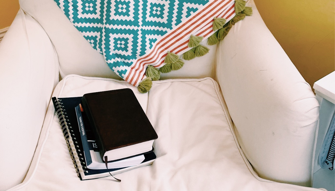 white chair against a yellow wall with a stack of books, including the Bible, on it