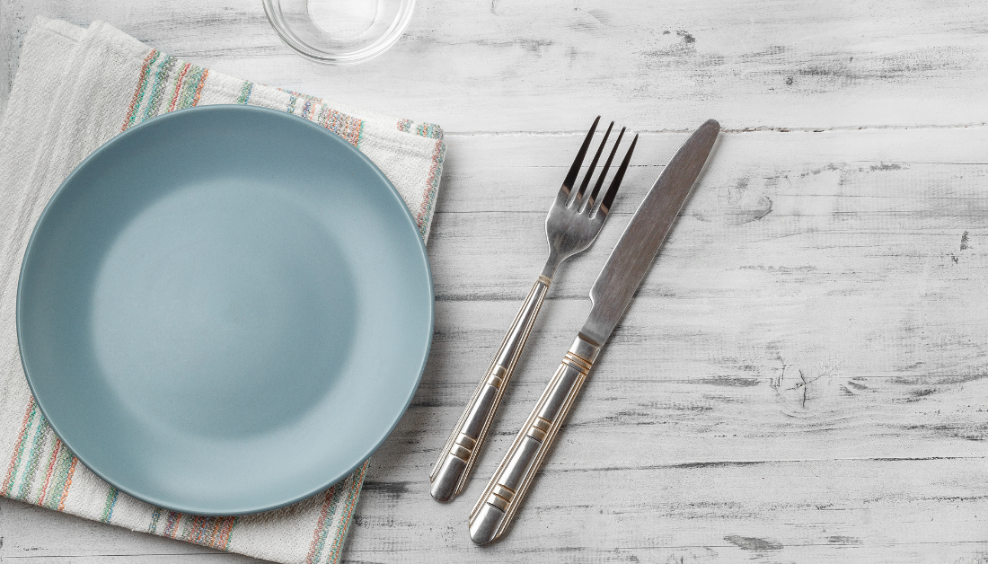 image is a plank table set with a blue plate, napkin, and fork and knife