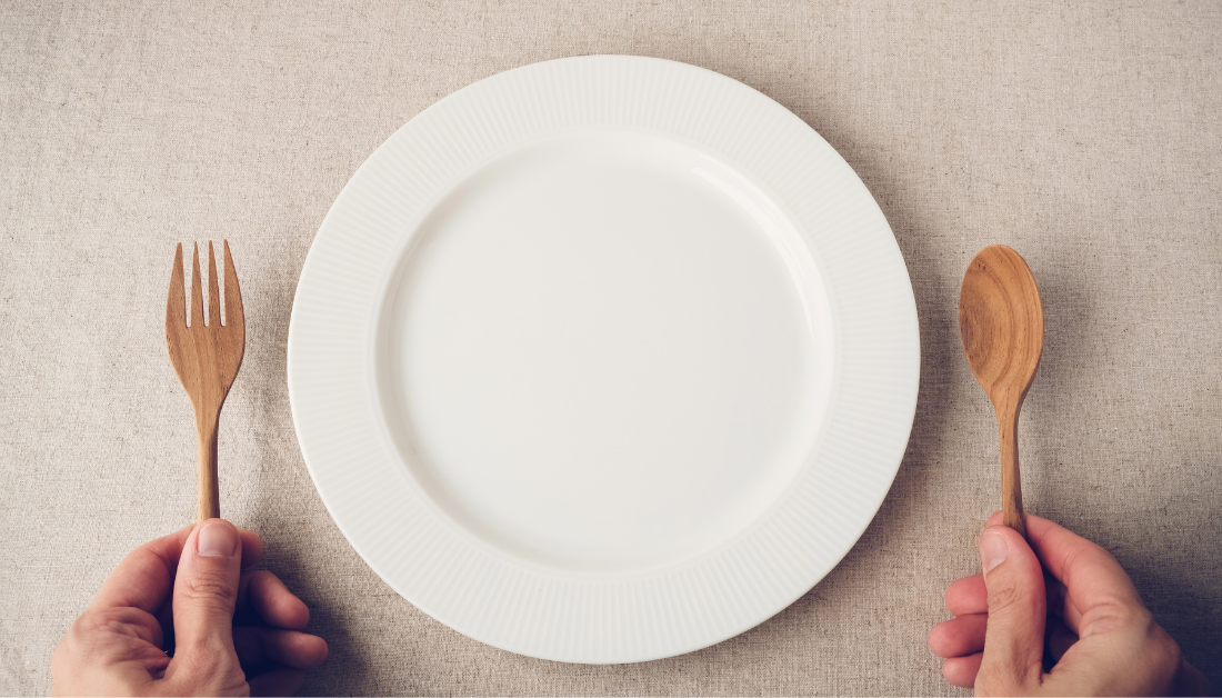 picture of empty white plate with hands holding wooden fork and spoon on either side of plate