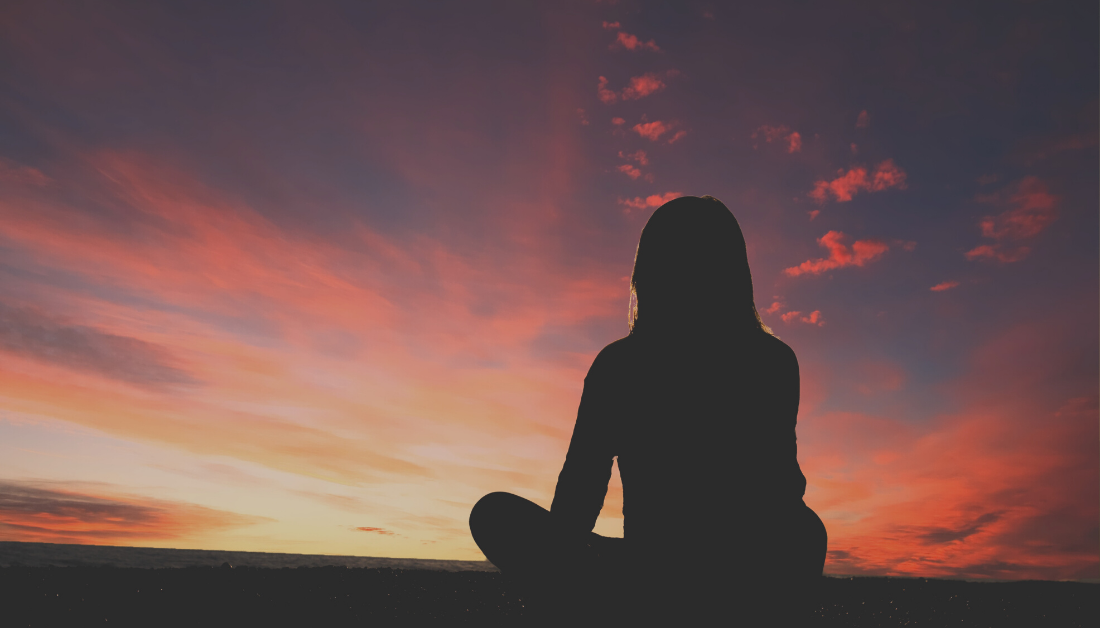image is a photo of a woman silhouetted against a sky with a pink sunset