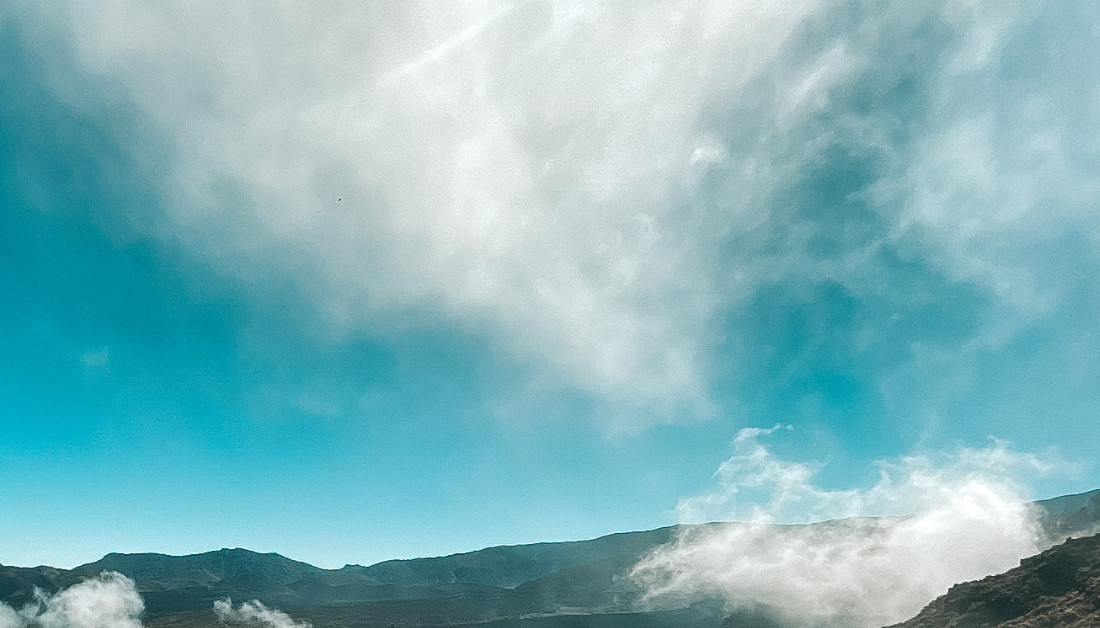 picture of the tops of mountains with wispy clouds above and below