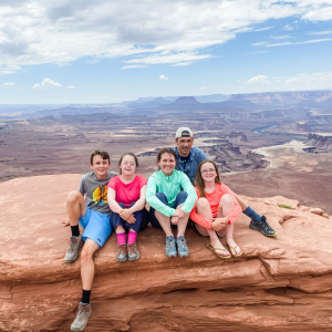 picture of family sitting on reddish rocks with canyons in the background