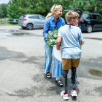a woman and a young boy with prosthetic legs carrying plants together