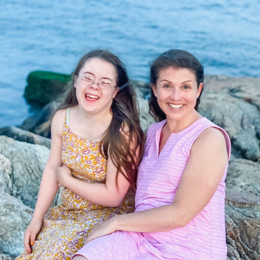 Penny and Amy Julia sitting on rocks next the ocean. Penny is laughing and Amy Julia is smiling at the camera