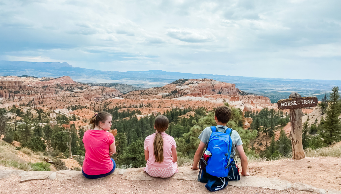 Penny, Marilee, and William sitting on a ledge with their backs to the camera and looking out over mountains looking contemplative