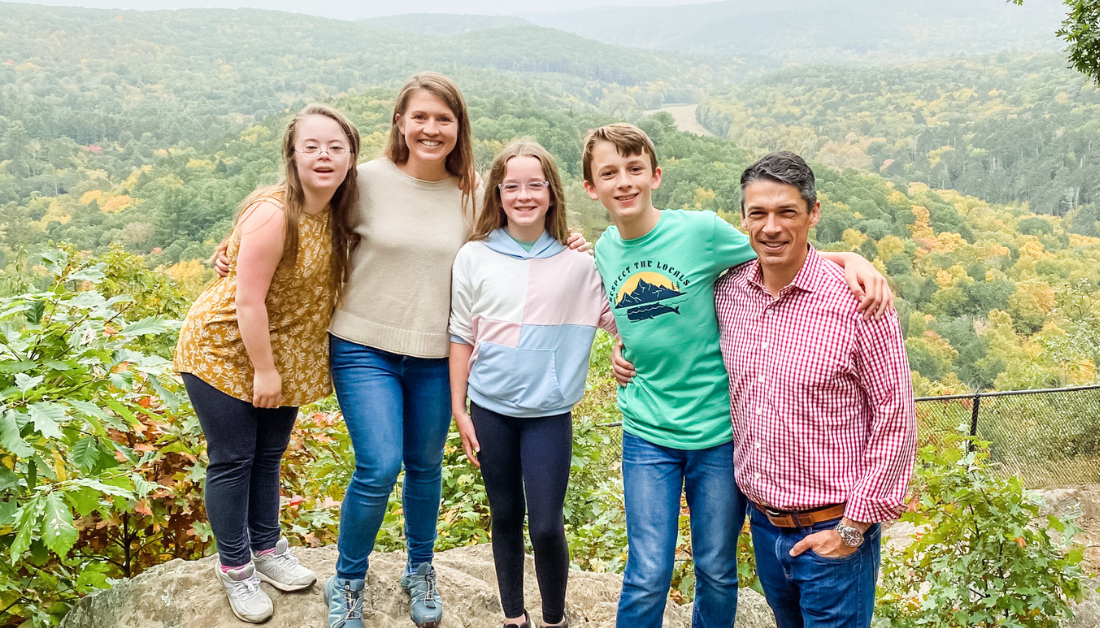 Amy Julia's family standing on an outcropping overlooking autumn trees far below