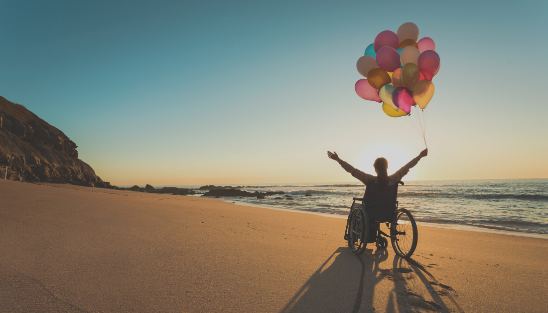 Person with a disability in a wheelchair with colored balloons at the beach