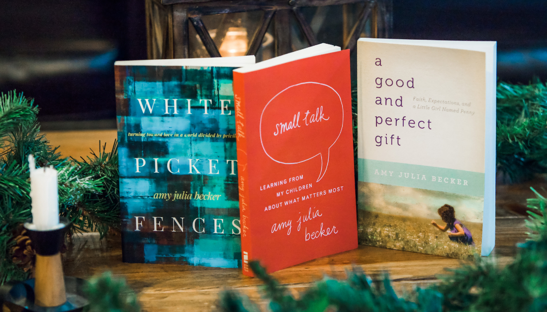 three books written by Amy Julia on a wooden table with a glowing lantern in the background