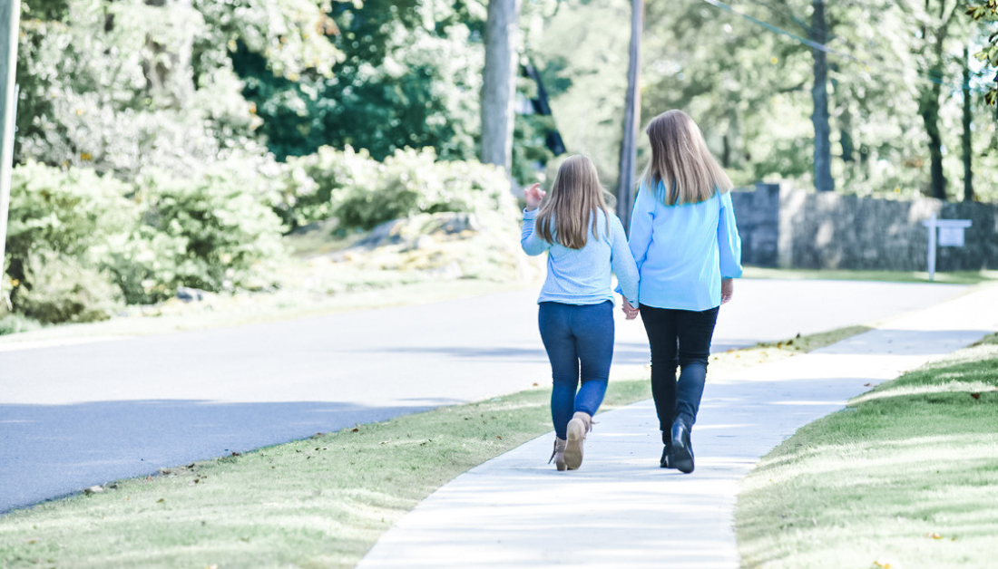 Penny and Amy Julia talking together as they walk away from the camera, following the curve of a sidewalk