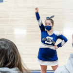 Penny in her cheerleading uniform cheering at a basketball game