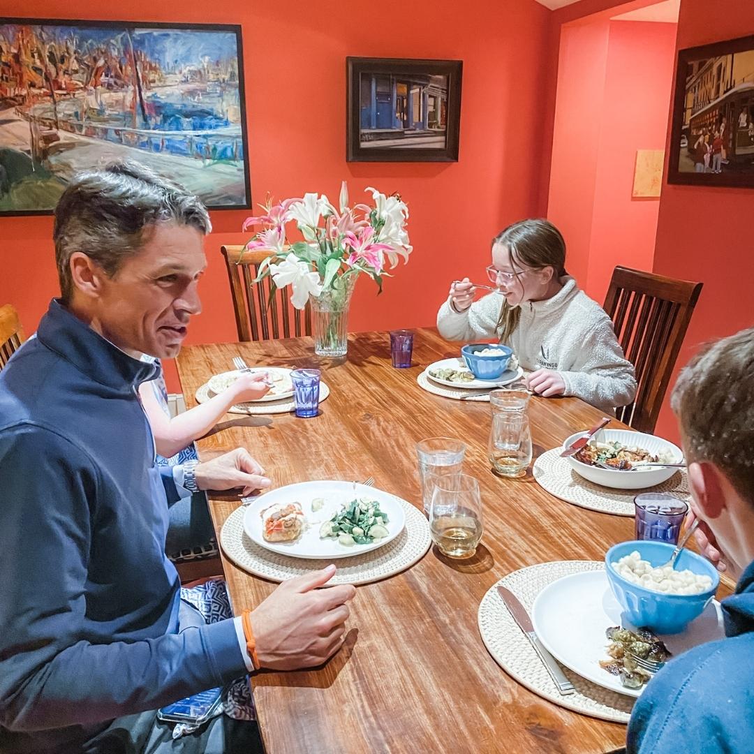 family sits at dining room table eating supper together