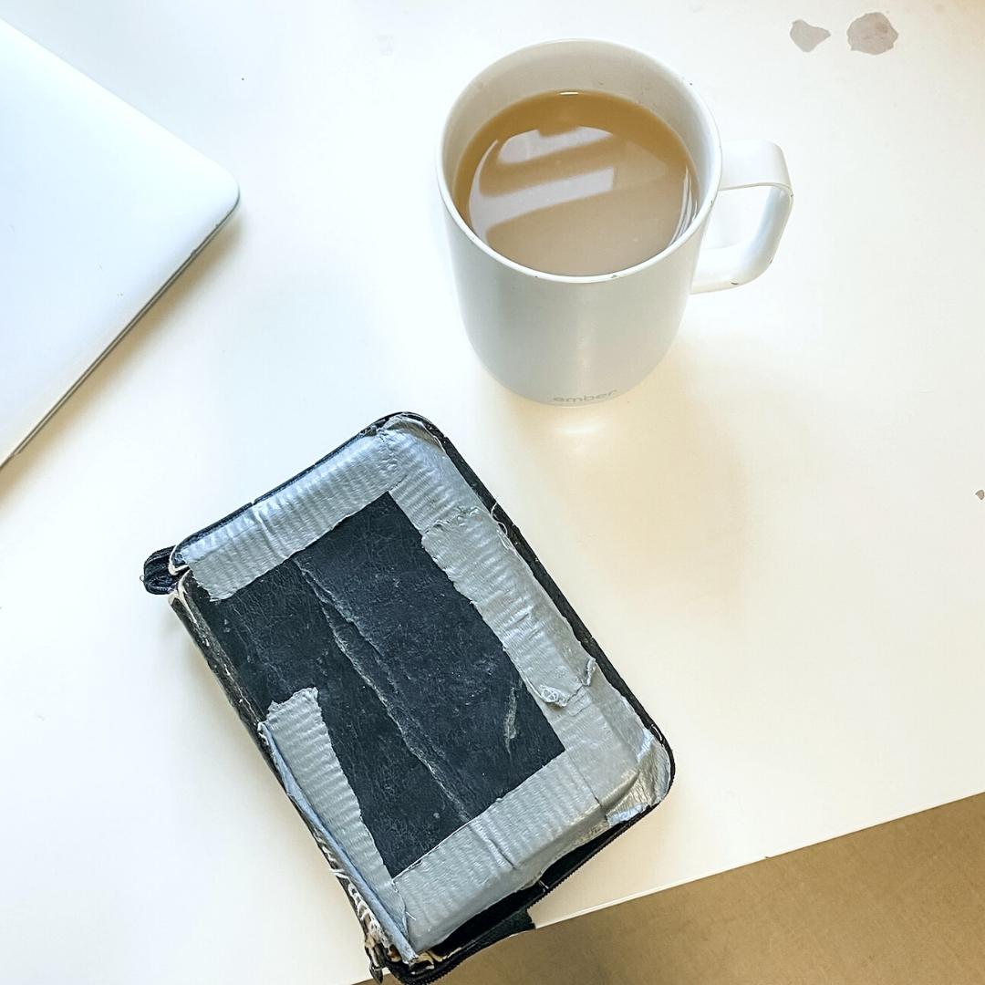 Looking down at a desk that has on it a cup of tea and a Bible that is duct taped