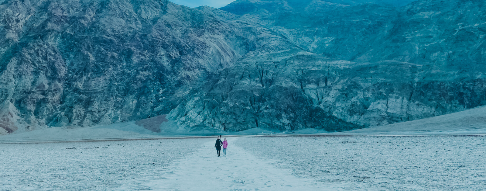 mountains in the background with people walking on a path in the distance across salt flats