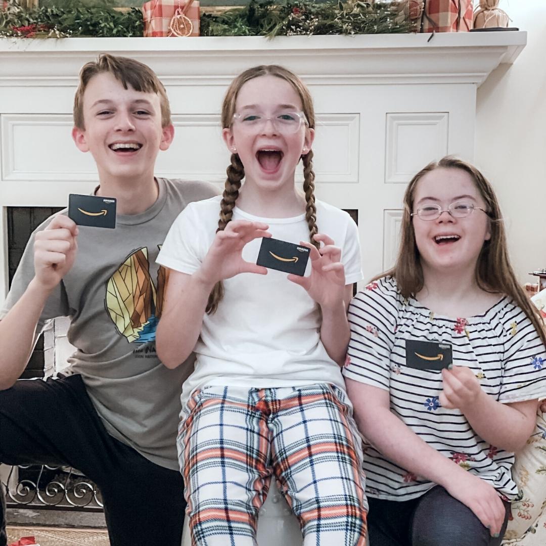 William, Marilee, and Penny smiling widely at the camera and holding Amazon gift cards