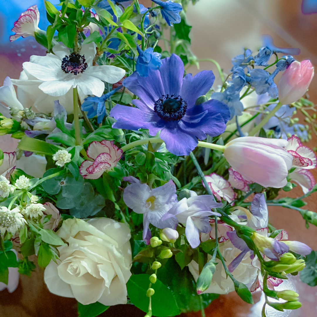 looking down at a vase of purple, white, and pale pink flowers in greenery