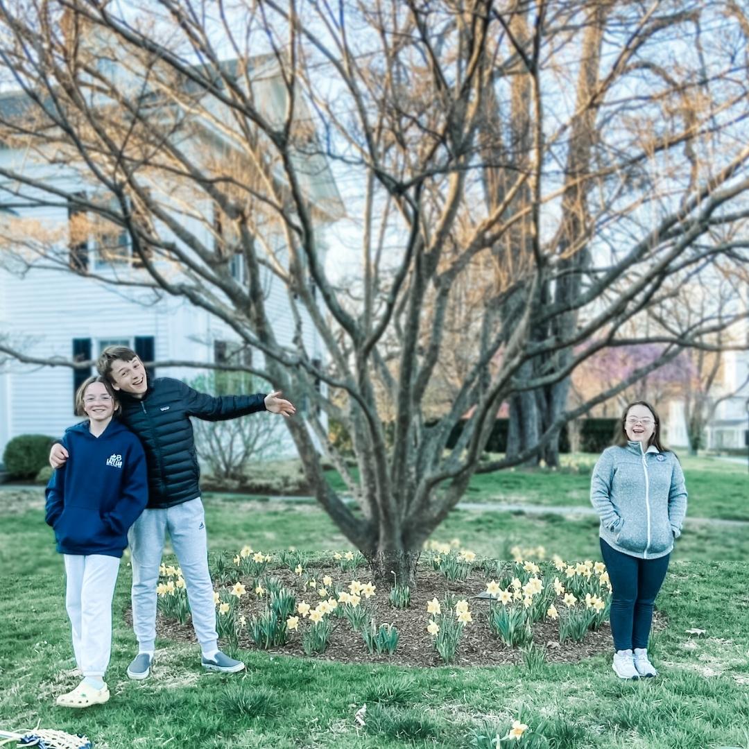 William and Marilee pose on one side of a tree, and Penny poses on the other side social distancing