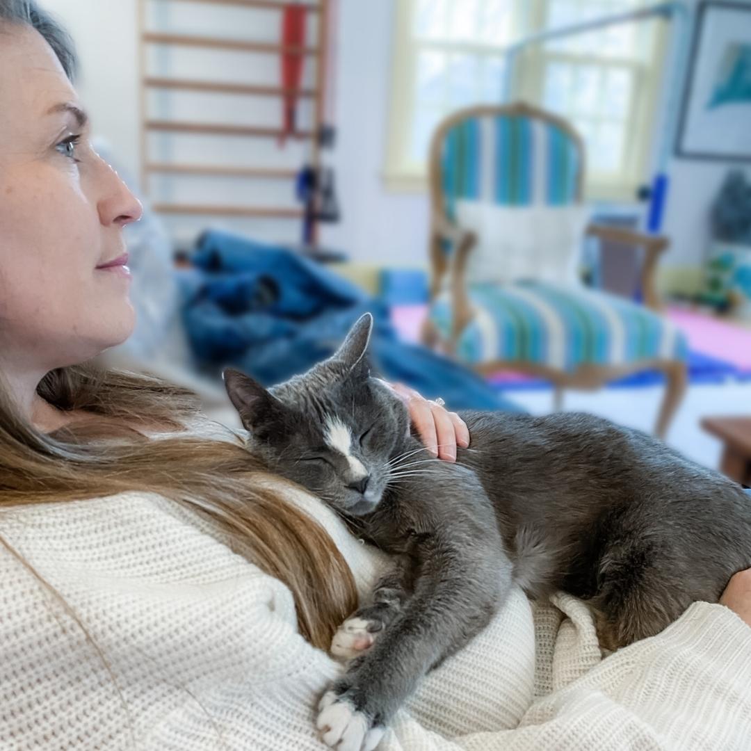 Amy Julis recovers from Covid. She looks across the room while she sits in a chair and holds her gray kitty on her chest