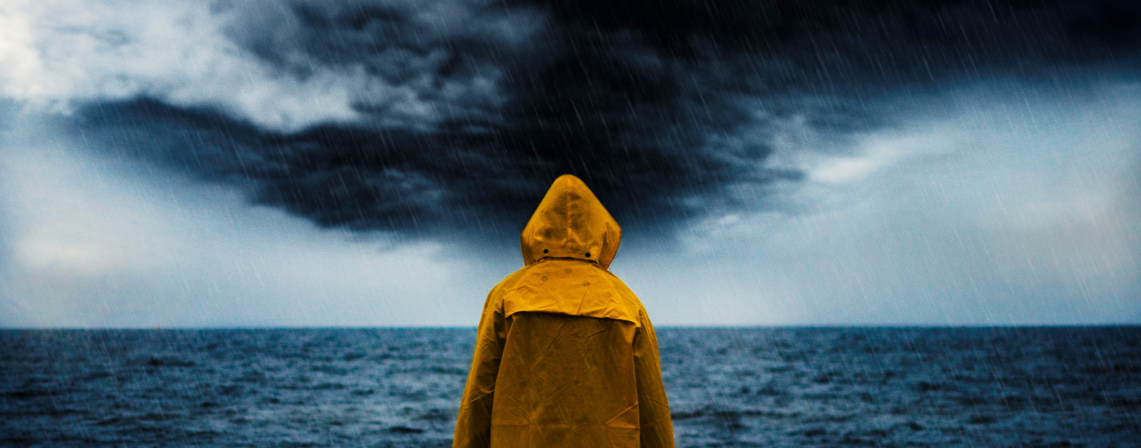 person wearing a yellow raincoat looking out at sea at an approaching storm, waiting