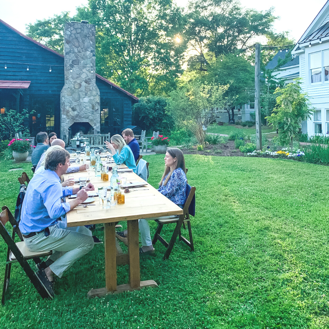 group of people eating outside at a long wooden table
