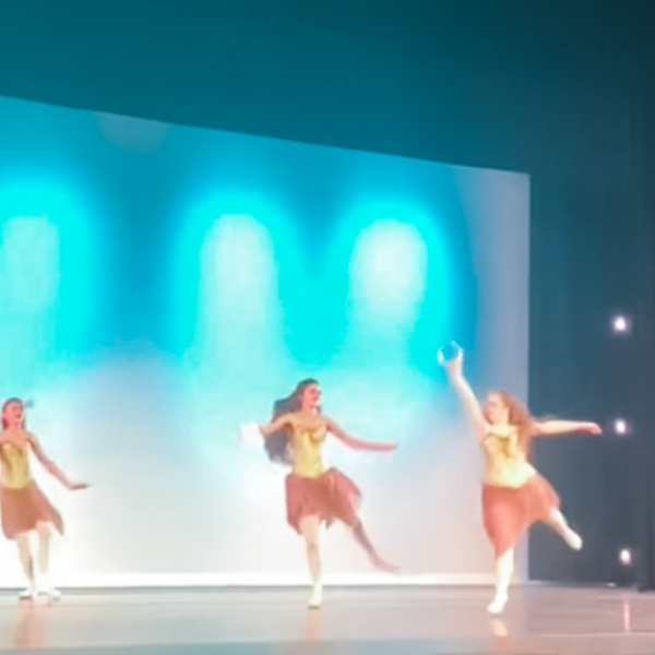 Penny dances on stage with other ballet dancers. Blue lights light up the stage backdrop.