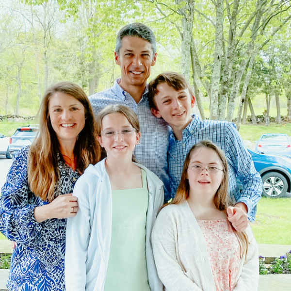 Becker family stands outside in front of a parking lot and low stone wall. They smile at the camera