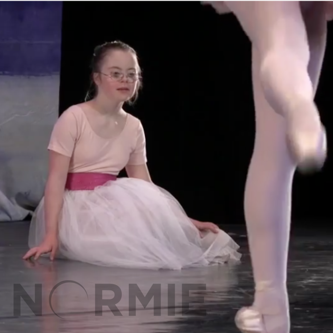 Penny is sitting on stage in a pink ballet costume. The picture was taken when she was several years younger. There is a "Normie" film logo overlay on the picture.