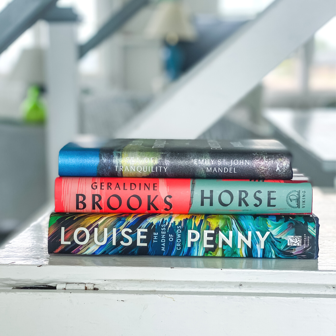 A stack of 3 books sits on a white staircase - The Sea of Tranquility, Horse, and The Madness of Crowds