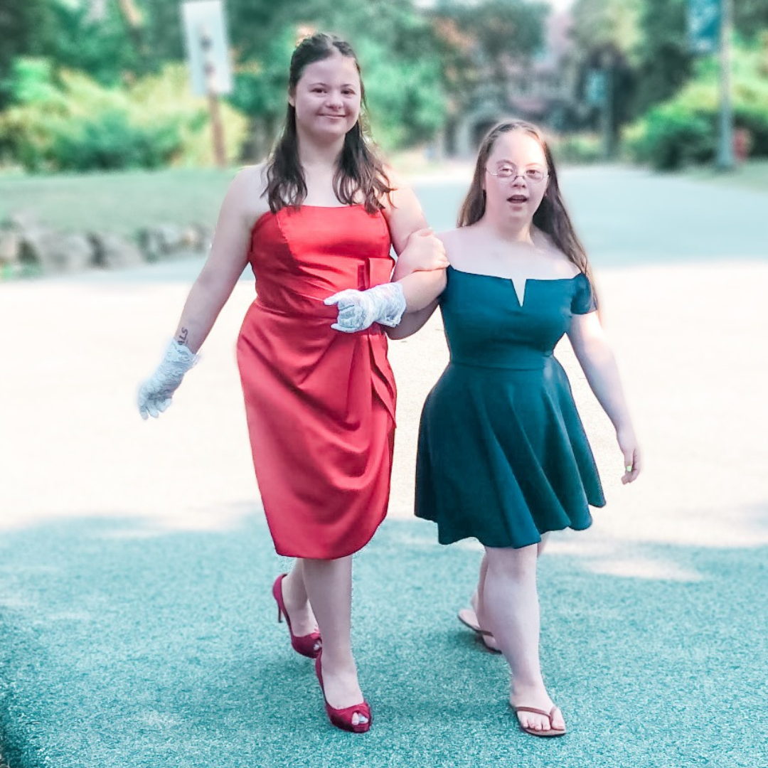 Penny's friend Rachel and Penny walk together arm in arm. They are wearing formal dresses.