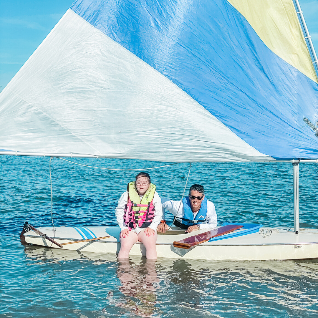 Penny and her dad sitting on a sailboat surrounded by the blue ocean