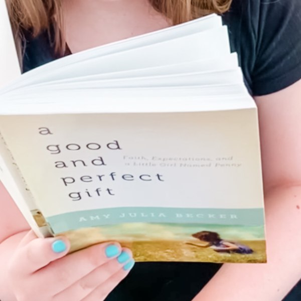 Penny's hand holding open a copy of A Good and Perfect Gift