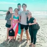 Amy Julia and family stand together on the beach with their arms around each other and the ocean in the background