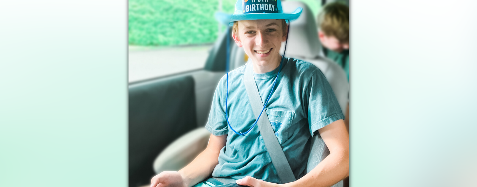 William sits in a van. He wears a blue hat that says, "It's my birthday."
