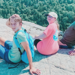 William, Penny, friend, and Marilee sit on a large rock with a forest far below them.