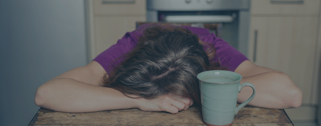 Tired Woman with Tea in Kitchen resting her head on her arms