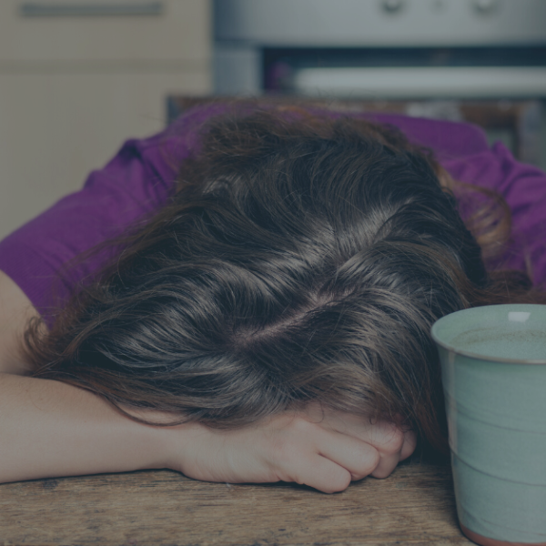 Tired Woman with Tea in Kitchen resting her head on her arms