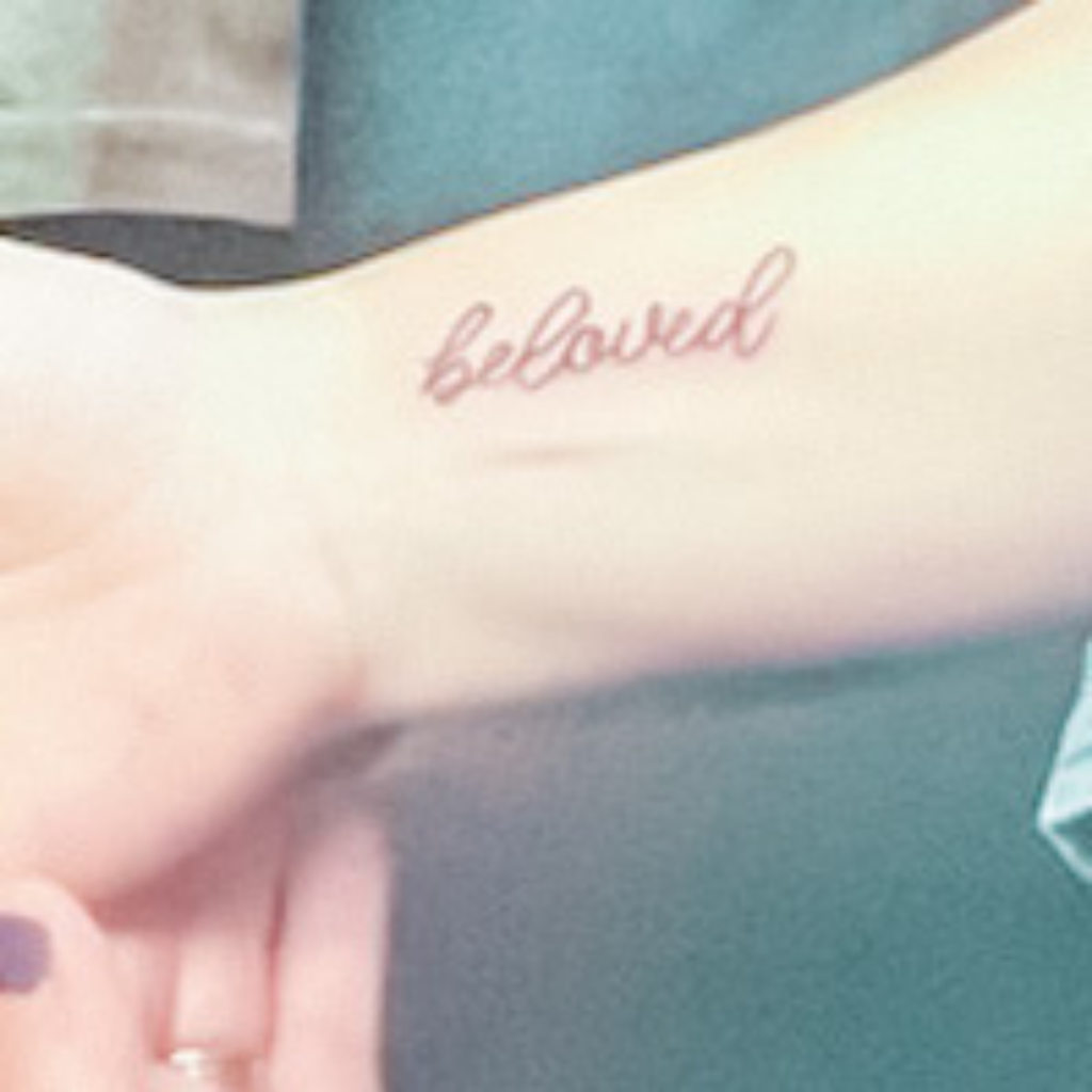 the word beloved tattooed on the inside of an arm in cursive script