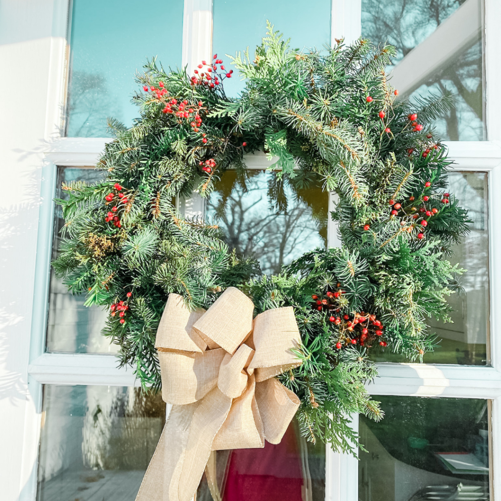 christmas wreath hangs on a white window pane