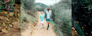 Penny and William hold hands and walk up a dirt, mountain path lined by brush