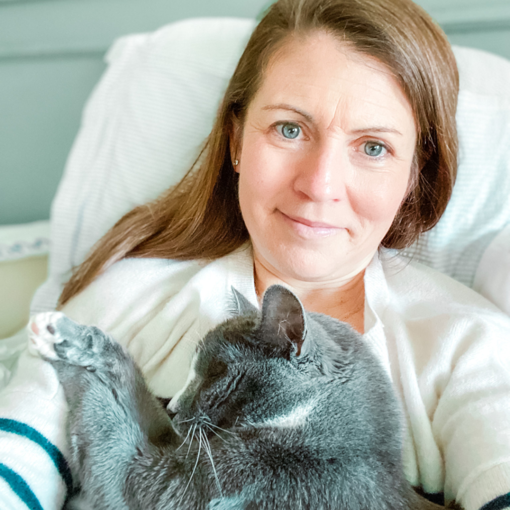 Amy Julia sits propped up in bed and holding a gray cat