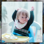 mosaic background behind a photo of one-year-old Penny raising her arms above her head. She is sitting in a high chair with cake on the tray.