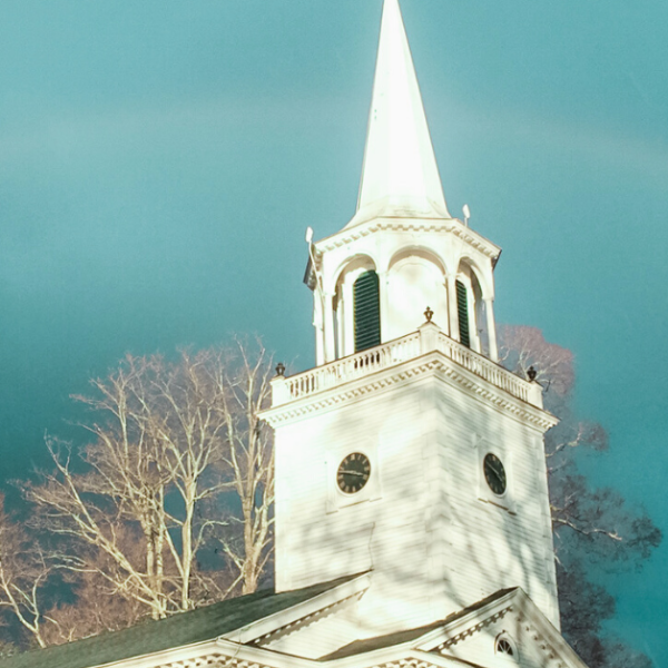 white church steeple against a dark blue sky with a rainbow behind