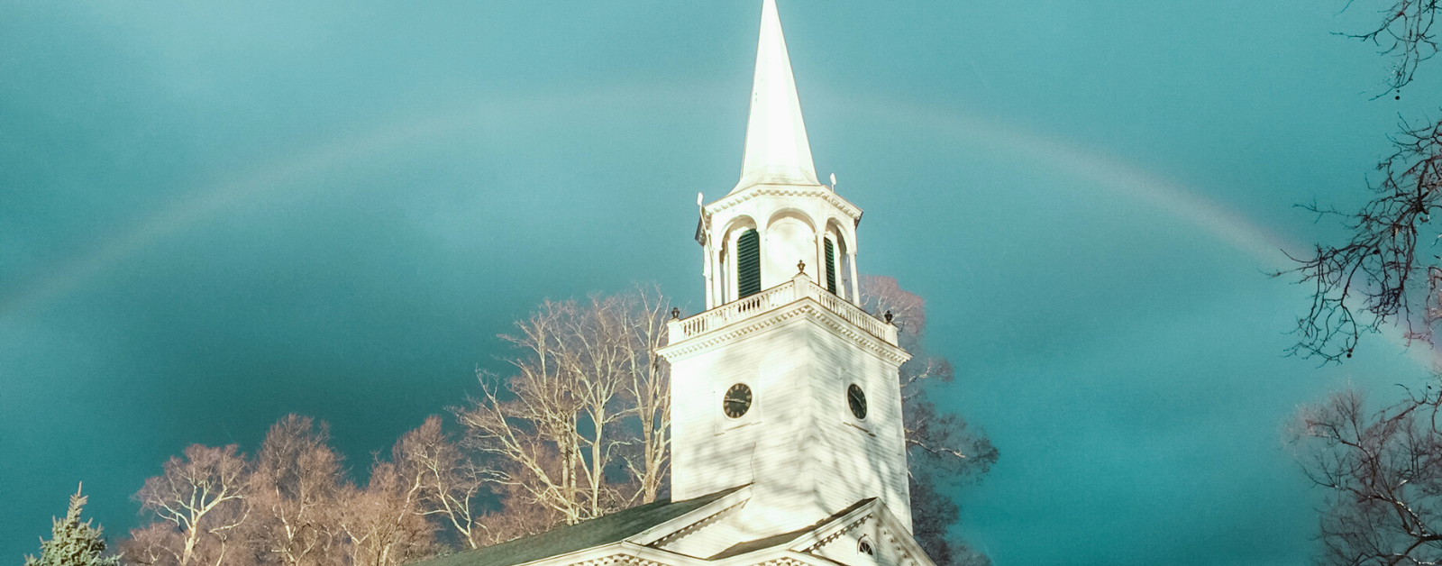 white church steeple against a dark blue sky with a rainbow behind