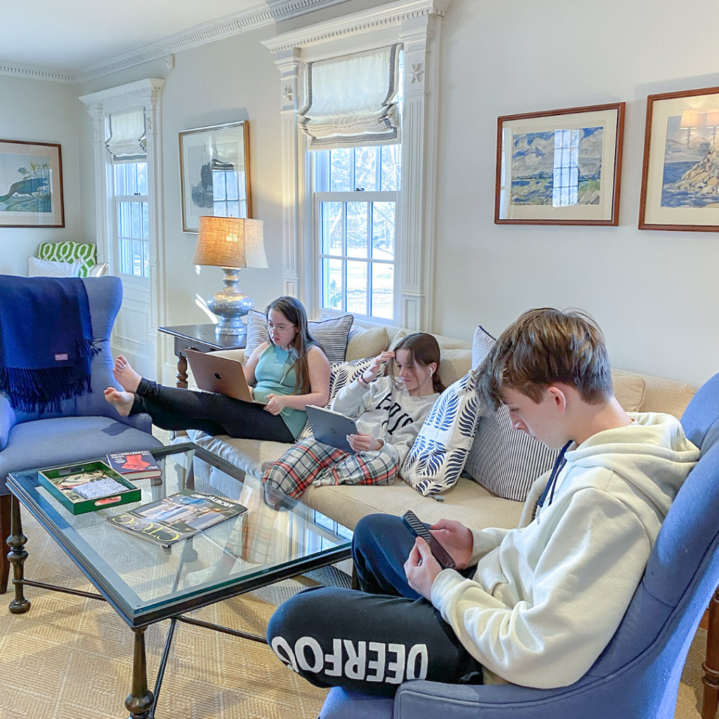 3 kids sit in a living room looking down at mobile devices