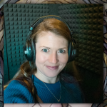 Amy Julia sits in a recording booth wearing head phones and smiling for a selfie
