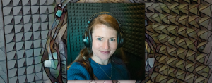 Amy Julia sits in a recording booth wearing head phones and smiling for a selfie