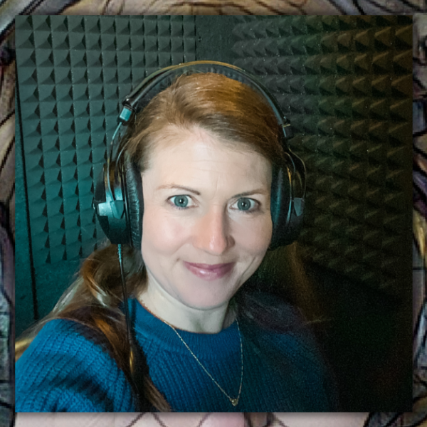 Amy Julia sits in a recording booth wearing head phones and smiling for a selfie