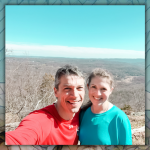 Peter and Amy Julia smile for a selfie while standing high above a valley