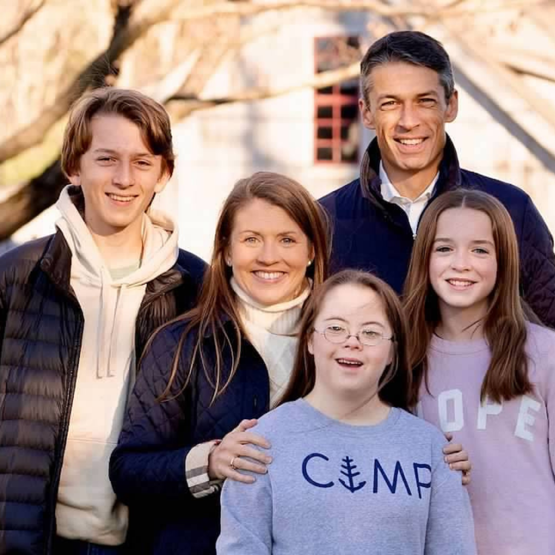 Becker family poses together outside. They are wearing jackets and sweatshirts and smiling at the camera