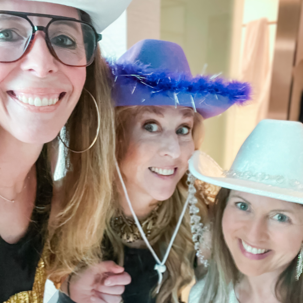 Amy Julia and two friends smile for a selfie and they are wearing cowboy hats