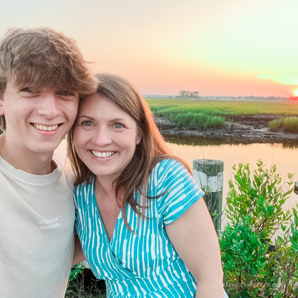 William and Amy Julia smile for a selfie with their heads together and a glowing sunset over water and hills behind them.